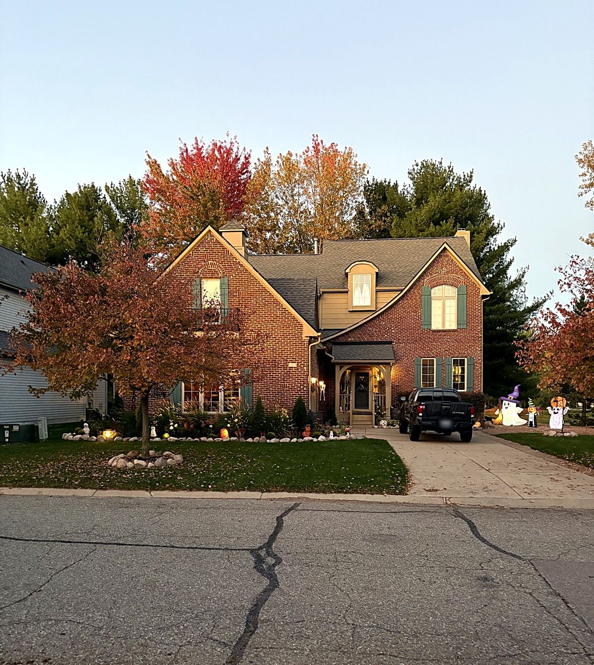 A brick two-story home at dusk, with fall maples and a landscaped front yard