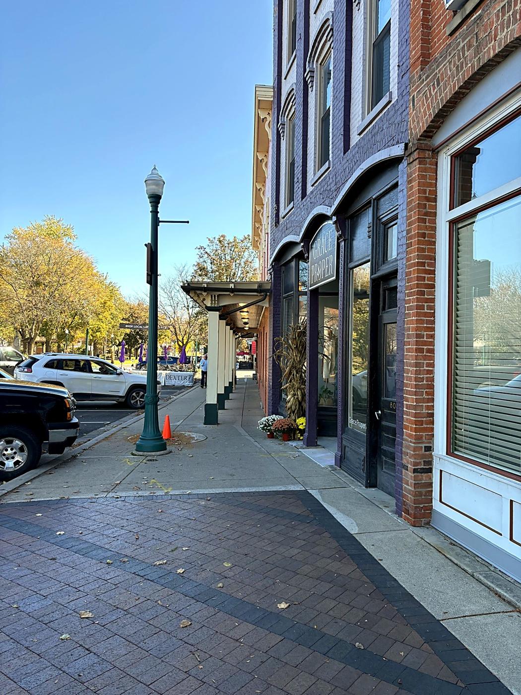 A brick sidewalk past storefronts in downtown Dexter